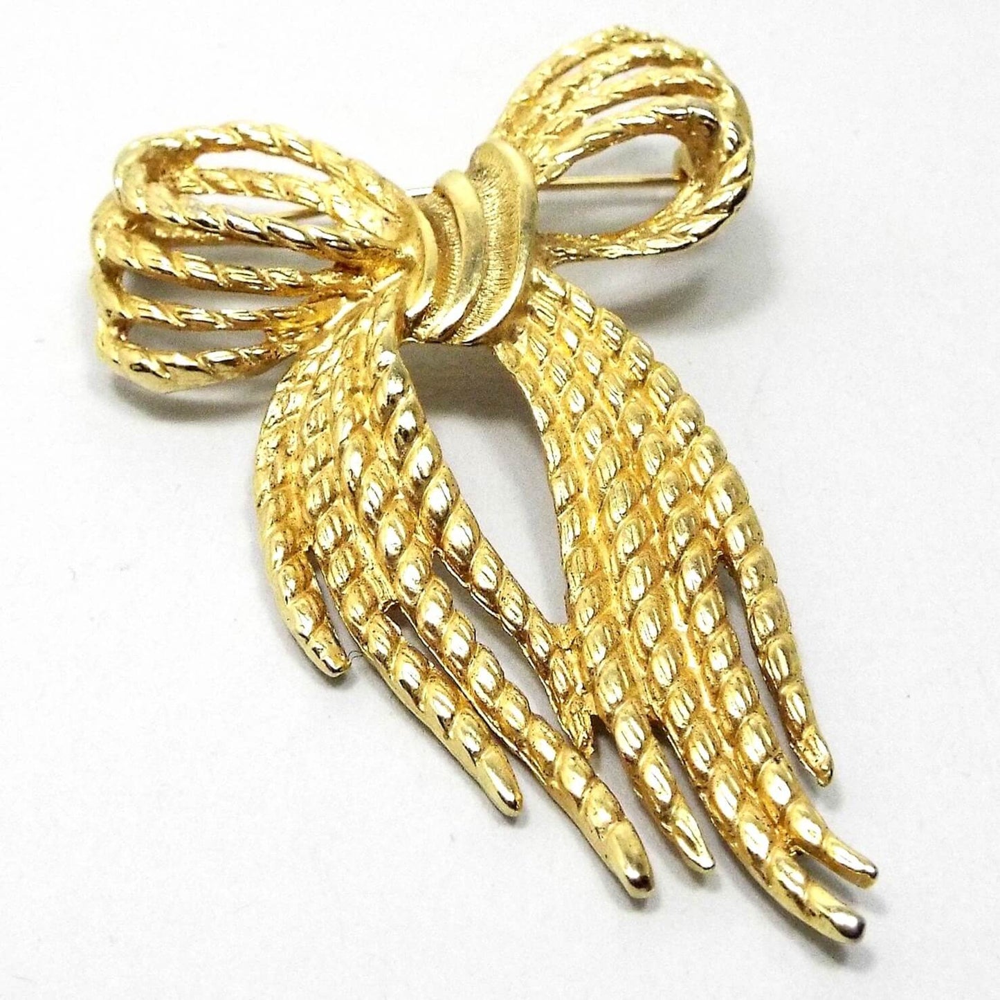 Front view of the retro vintage bow brooch. The metal is gold tone in color and has a textured appearance. It is shaped like a tied Holiday bow.