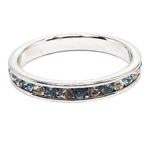 Angled view of the retro vintage rhinestone eternity band ring. It is a thinner style band with silver tone color metal. There is a channel that goes all the way around the band and has alternating light blue and clear rhinestones in it.