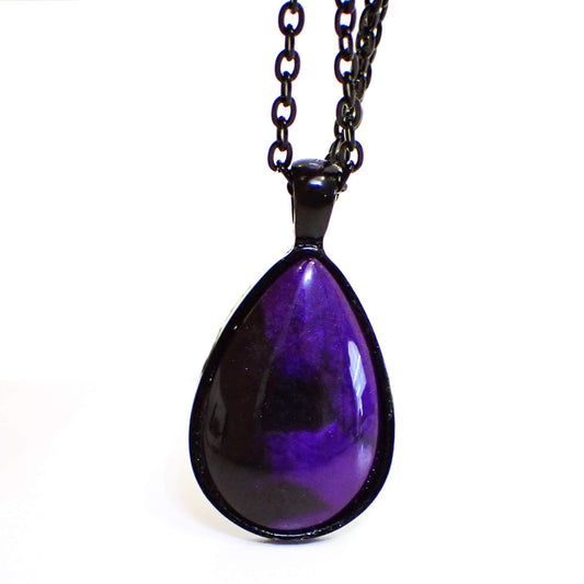 Enlarged front view of the Goth handmade resin teardrop pendant necklace. The metal is black coated. The teardrop has a resin cab on the front that has marbled pearly black and pearly deep purple resin. 