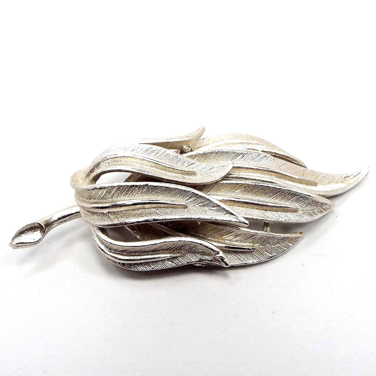 Front view of the Coro Mid Century vintage branch brooch pin. It is silver tone in color with a matte textured design of long leaves on the end.
