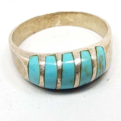 Angled front and side view of the retro vintage magnesite band ring. The sterling silver is slightly darkened from age. There are 5 bands of inlaid blue dyed magnesite gemstone on the top. The top is slightly domed and curved. The magnesite is a light faux turquoise blue in color. 