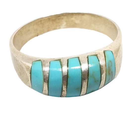 Angled front and side view of the retro vintage magnesite band ring. The sterling silver is slightly darkened from age. There are 5 bands of inlaid blue dyed magnesite gemstone on the top. The top is slightly domed and curved. The magnesite is a light faux turquoise blue in color. 