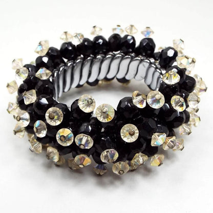 Angled side view of the Mid Century vintage beaded expansion bracelet. It is heavily beaded with faceted black oval beads that have AB crystal saucer beads on top. There are silver tone metal links on the inside that expand for size.