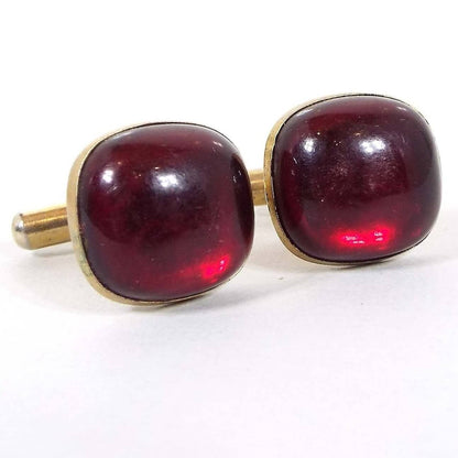 Front view of the Mid Century vintage lucite cufflinks. The metal is gold tone in color and they have a rounded square shape. The fronts have domed red lucite cabs that are semi translucent.