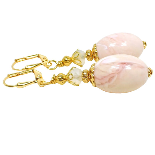 Side view of the handmade earrings with oval vintage lucite beads. The metal is gold plated in color. There are faceted glass crystal beads in a semi translucent opal white color on top. The bottom lucite beads have swirled shades of light pink and peach.