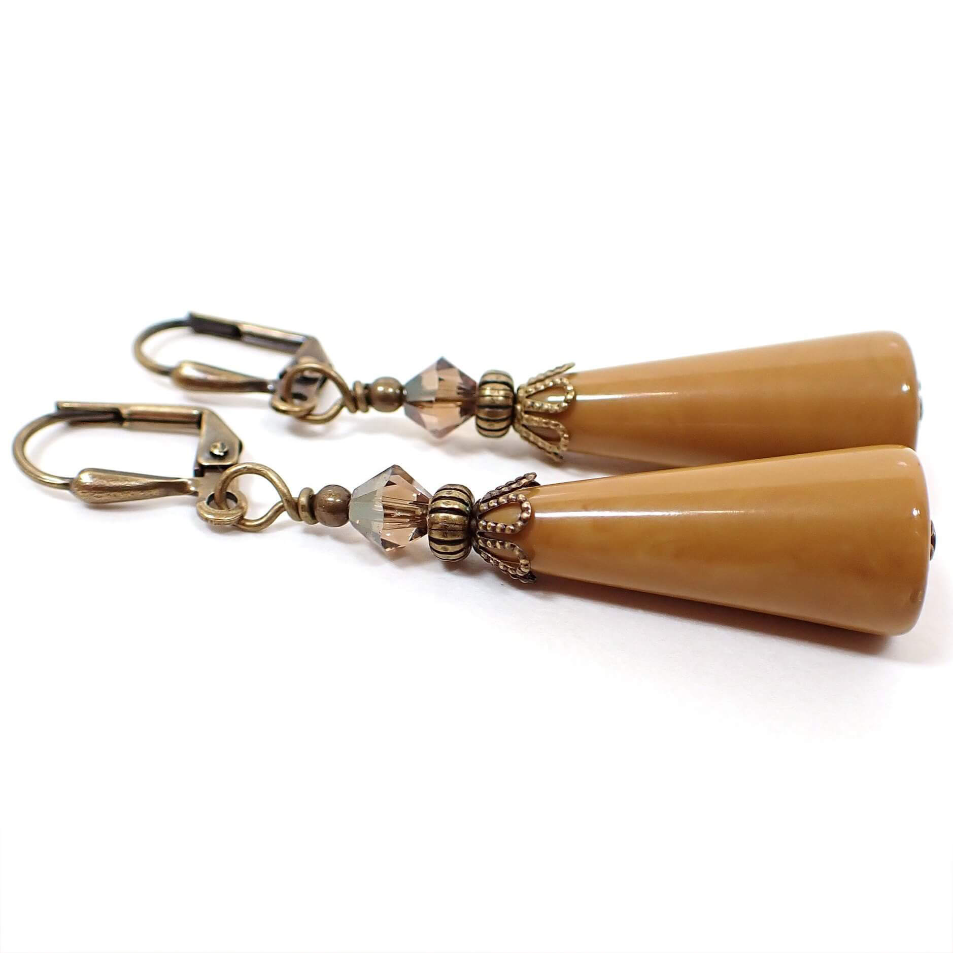 Side view of the handmade cone earrings. The metal is antiqued brass in color. There are faceted brown bicone beads at the top and cone shaped lucite beads at the bottom in a light brown color.