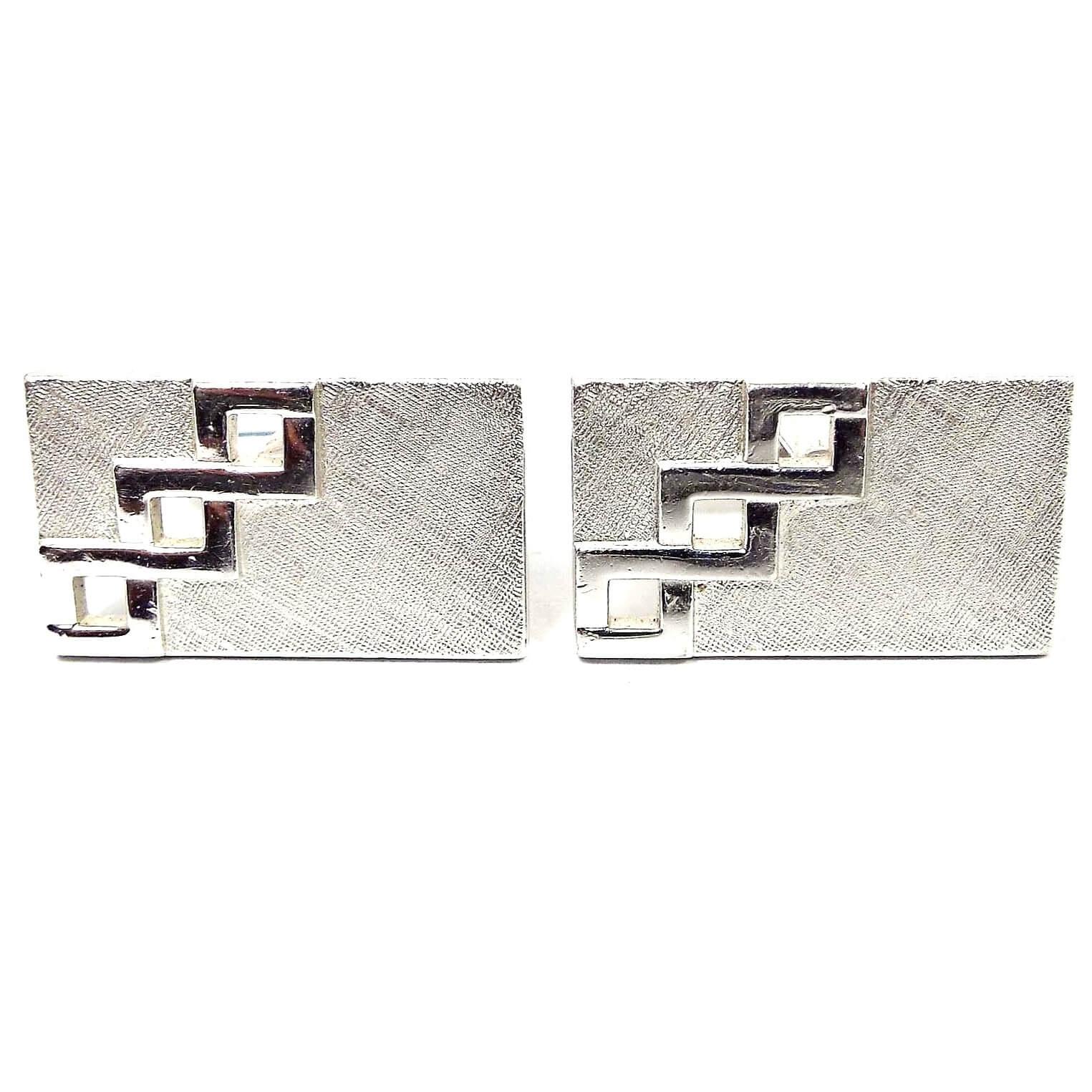 Front view of the Mid Century vintage Swank cut out cufflinks. They are rectangle in shape and have textured matte silver tone color fronts. There is a cut out design with three squares going diagonally on one side of each cufflink.