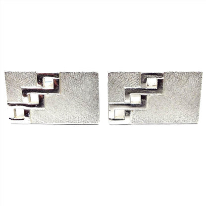 Front view of the Mid Century vintage Swank cut out cufflinks. They are rectangle in shape and have textured matte silver tone color fronts. There is a cut out design with three squares going diagonally on one side of each cufflink.