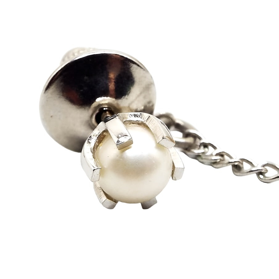 Enlarged view of the Sarah Coventry retro vintage cultured pearl tie tack. The metal is silver tone in color. There is a white round pearl in the middle of a prong setting. 