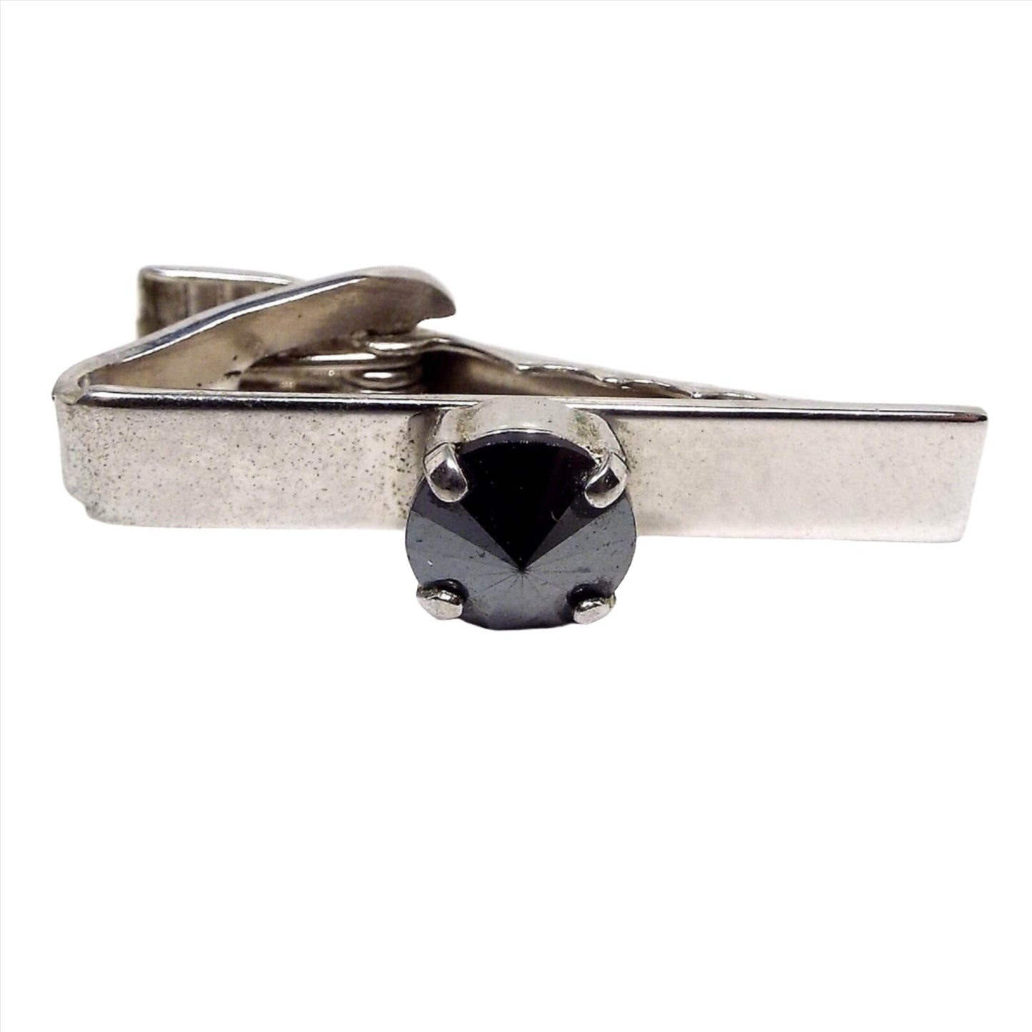 Front view of the Mid Century vintage faux hematite tie clip. The metal is silver tone in color. In the middle is a prong set rivoili rhinestone that is dark metallic gray in color.