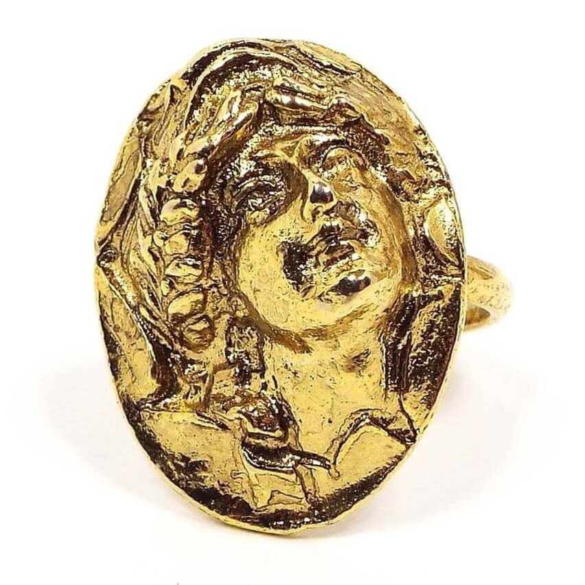 Front view of the retro vintage Vogue cameo adjustable ring. The metal is an antiqued gold in color. The front has a raised repousse cameo of a lady's face on an oval setting.