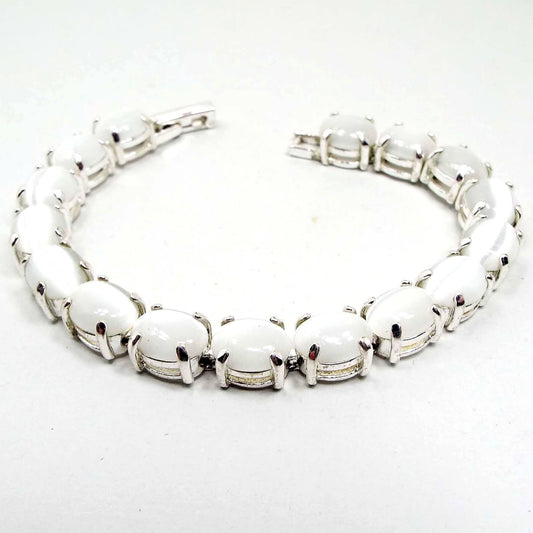 Angled view of the retro vintage faux cat's eye link bracelet. The metal is silver tone in color. There are oval white glass cabs on each link that are imitation cat's eye and have a glowy effect as you move around in the light.