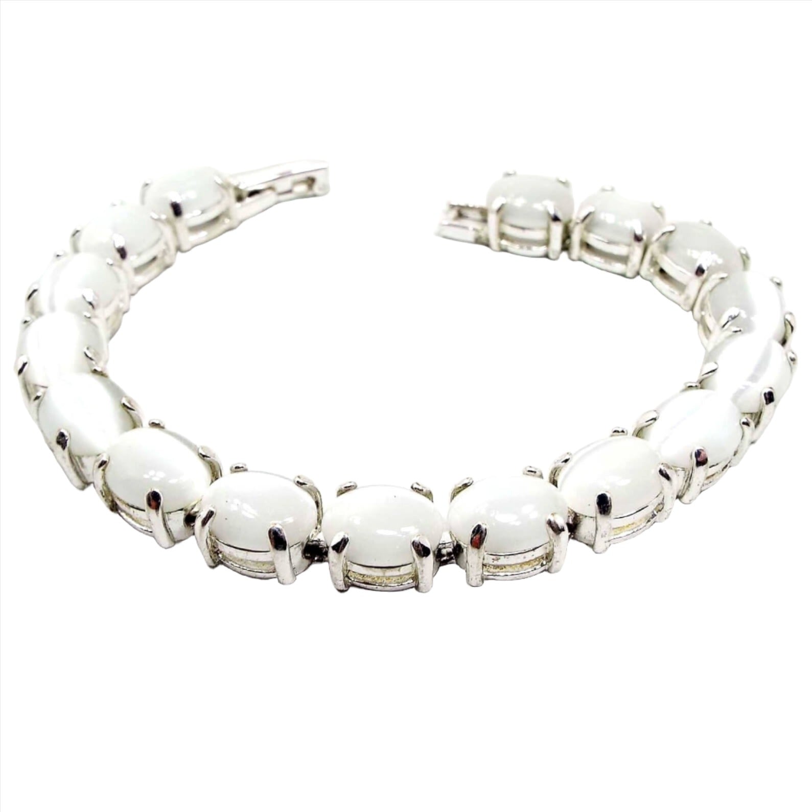 Angled view of the retro vintage faux cat's eye link bracelet. The metal is silver tone in color. There are oval white glass cabs on each link that are imitation cat's eye and have a glowy effect as you move around in the light.