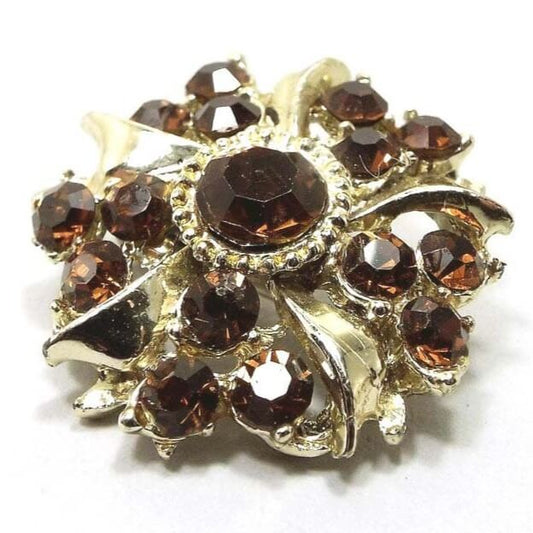 Front view of the Mid Century vintage rhinestone brooch pin. The metal is gold tone in color and has a starburst sort of shape. There is a brown rhinestone in the middle with smaller sized brown rhinestones around it in groups of three.