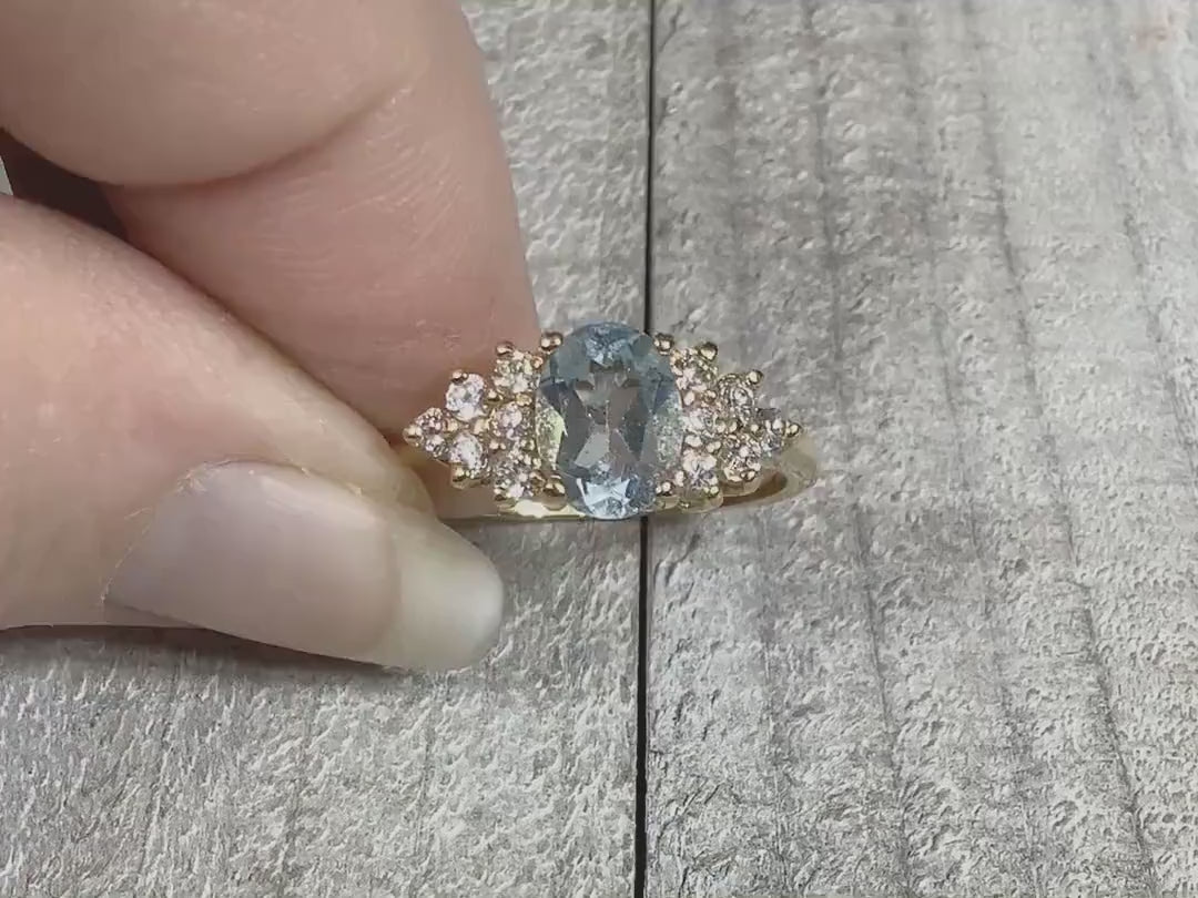 Video of the retro vintage cocktail ring and how the stones sparkle. The metal is light gold tone in color. There is an oval light blue topaz stone at the top with small round clear cubic zirconia stones on the sides.