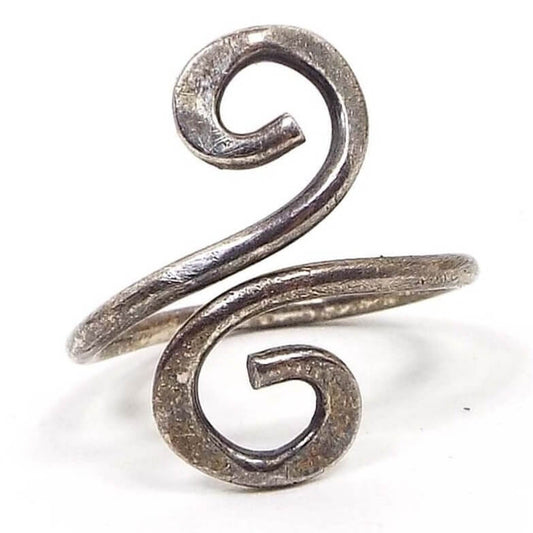 Front view of the retro vintage bypass ring. The silver tone metal is darkened from age. The ring is made from rounded thick wire and bypasses up at the top with each side curling around in opposite directions. The ends are hammered to flatten then some. 