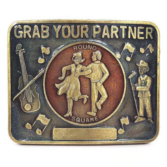 Front view of the retro vintage square dancing belt buckle. The metal is antiqued brass in color. It has a blue enameled area with Grab Your Partner, musical notes, and a square dancing caller. In the middle is a red enameled area that says Round Square with a couple dancing. There is a plain rectangle plate at the bottom.
