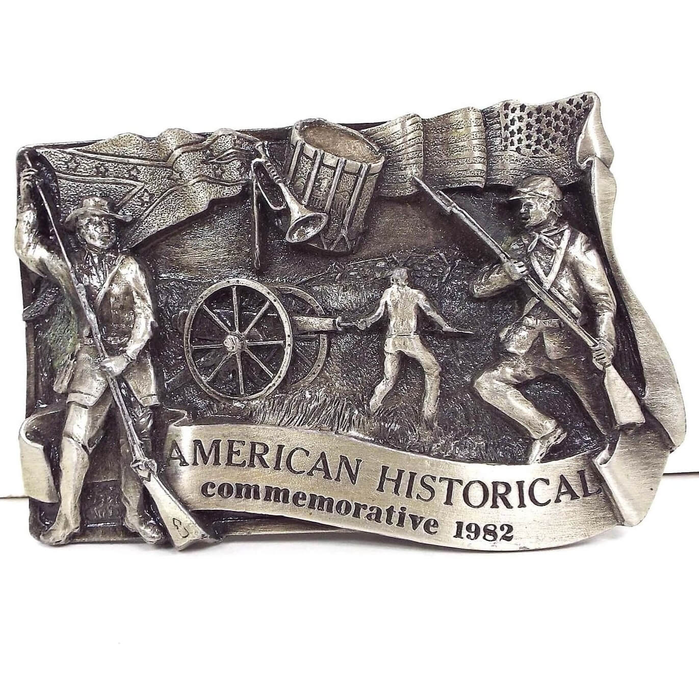 Front view of the retro vintage Siskiyou American Historical Commemorative belt buckle. It shows a soldier from each side of the civil war as well as someone loading a cannon in the middle. It's marked 1982 on the front.