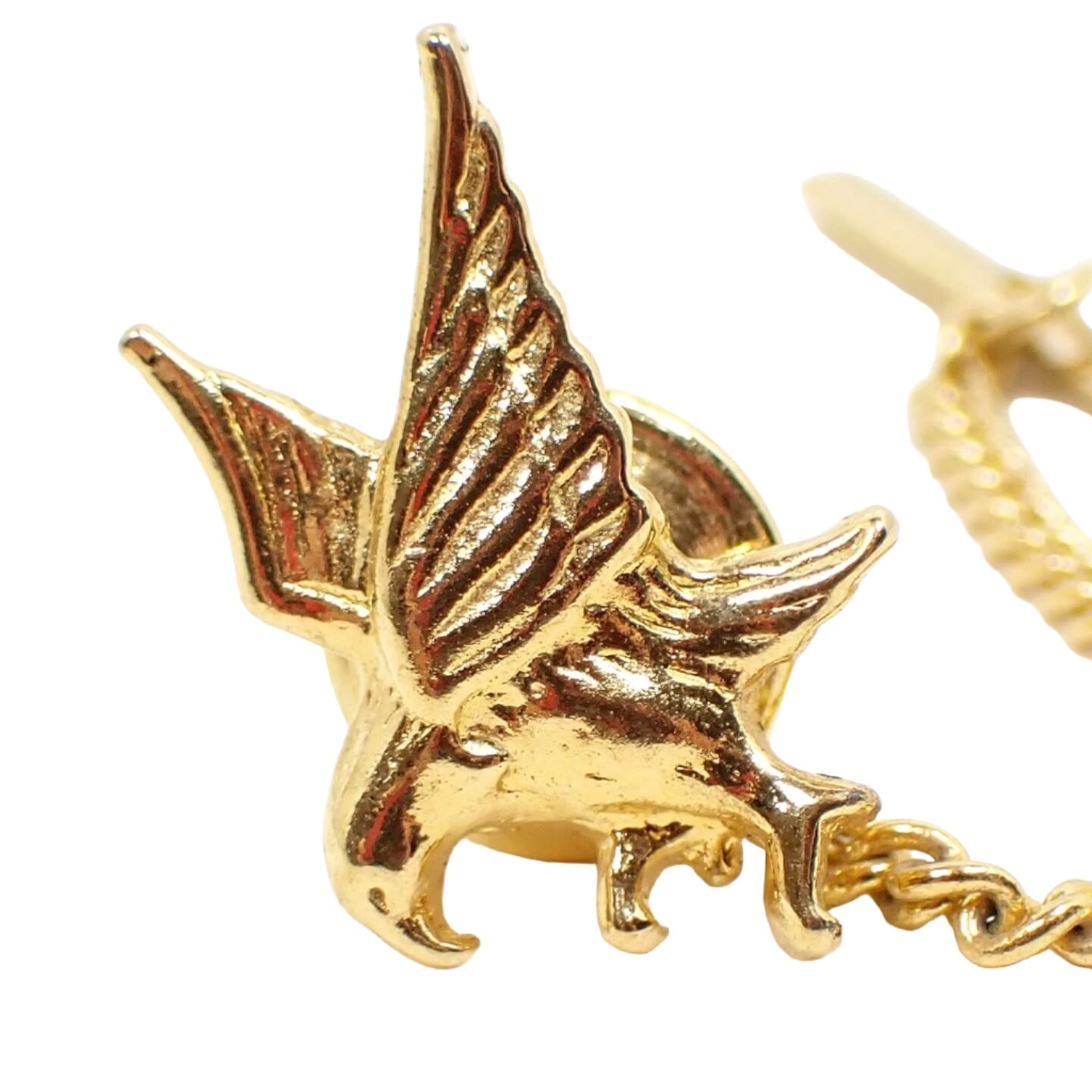 Enlarged front view of the retro vintage eagle tie tack. The metal is gold tone plated in color. The tie tack is shaped like a flying eagle with its sings out and talons spread to grab something or land.