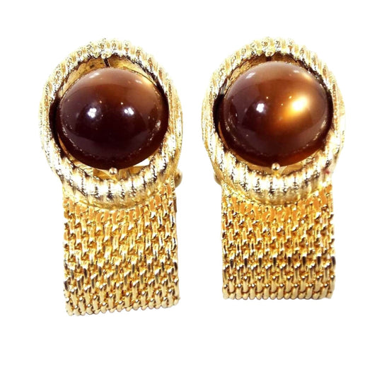 Front view of the Swank Mid Century vintage wrap around cufflinks with moonglow lucite. The metal is gold tone in color. There is wide mesh coming from the bottom that goes around to the backs. The tops are oval shaped with round domed moonglow lucite cabs in a rich golden brown color.