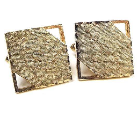 Front view of the Mid Century vintage square cufflinks. They are gold tone in color with matte brushed textured fronts. Two corners have a cut out area. There is a faceted edge on the other two corners.