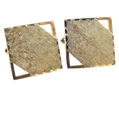 Front view of the Mid Century vintage square cufflinks. They are gold tone in color with matte brushed textured fronts. Two corners have a cut out area. There is a faceted edge on the other two corners.