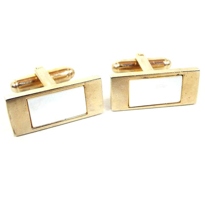 Angled front view of the Mid Century vintage mother of pearl cufflinks. They are rectangle with gold tone color metal. There are inlaid rectangle pearly white mother of pearl cabs in the middle.