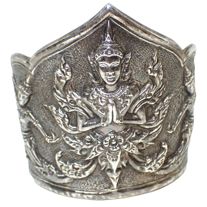 Front view of the Mid Century 1940's Vintage Siam Thai cuff bracelet. It is dark gray color sterling silver in color. It has a rounded bottom edge and the top has a rounded edge on each side and a point in the very middle. The front has a raised depiction of Hindu Goddess and you can see part of the design of the raised dancers on the side.