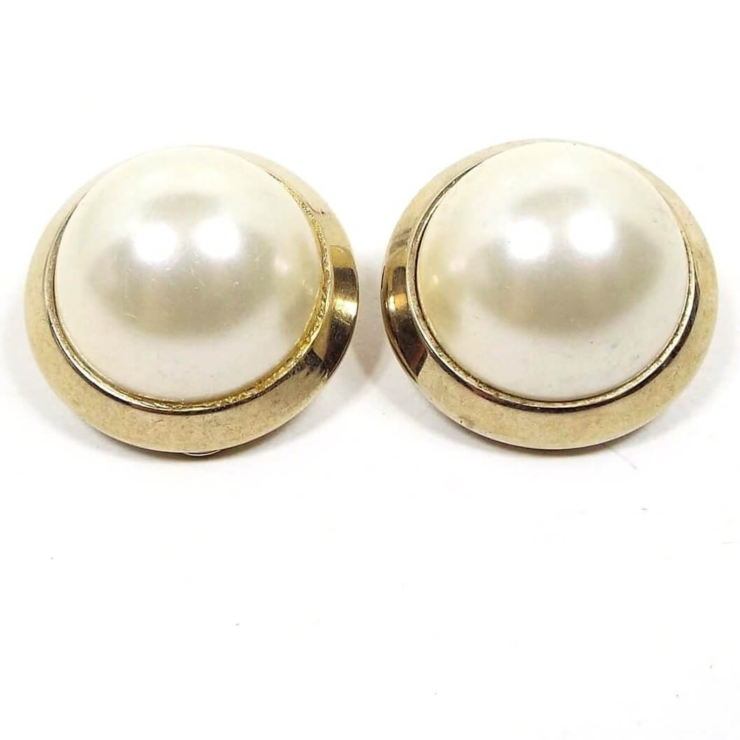 Front view of the retro vintage Marvella faux pearl earrings. They are round and gold tone in color with domed off white plastic imitation pearl fronts.