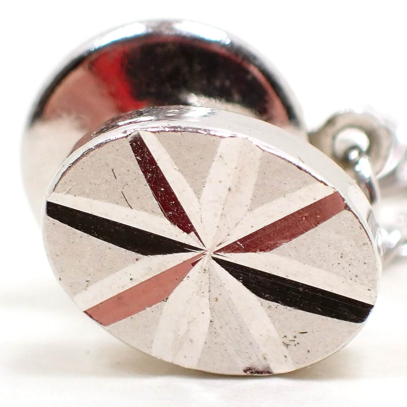 Enlarged front view of the Mid Century vintage starburst tie tack. It is oval in shape and silver tone plated in color. There is a cut etched starburst design on it.