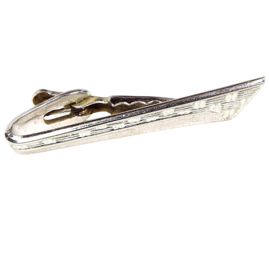 Front view of the Mid Century vintage Shields Modernist style tie clip. It is silver tone in color and has a textured pattern on the top part of the front with a thin curve design on the bottom. The end is angled and flares out at the top. 