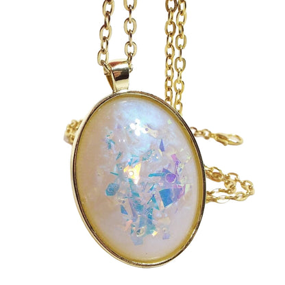 Front view of the handmade oval resin pendant necklace. The metal is gold tone in color. The oval pendant has a domed cab with color shift resin that has shades of pearly off white and blue. There are large chunks of AB glitter with blue, purple, and pink hues showing inside the resin for flashes of color.