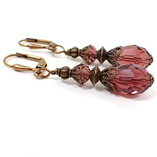 Side view of the handmade glass crystal teardrop earrings. The metal is antiqued brass in color. There are glass crystal beads at the top and bottom in a wine purple color with filigree bead caps. The bottom beads are teardrop shaped.