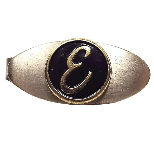 Front view of the retro vintage initial tie clip. It is a small oval that's gold tone in color and has a black enameled circle in the middle with the letter E in it.