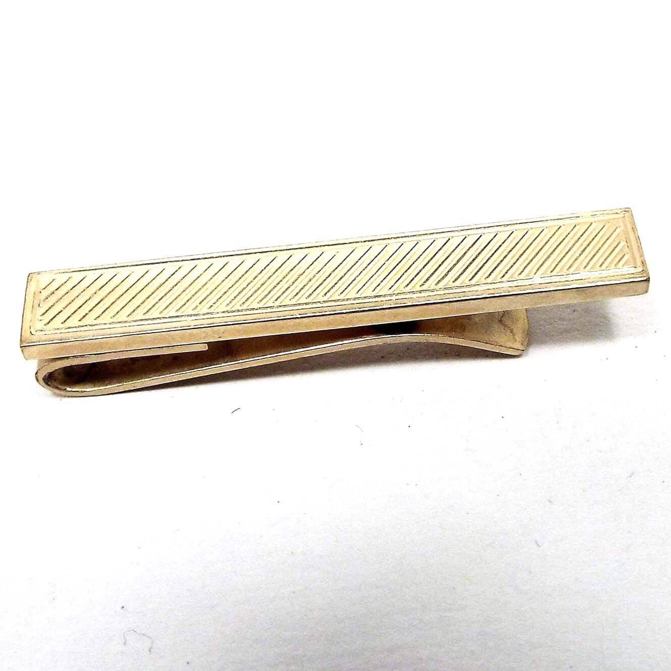 Front view of the Mid Century vintage Dante gold filled tie bar. The metal is gold in color and rectangular shaped. There is an etched diagonal line design down the tie bar.