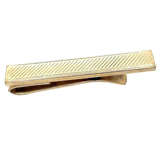 Front view of the Mid Century vintage Dante gold filled tie bar. The metal is gold in color and rectangular shaped. There is an etched diagonal line design down the tie bar.