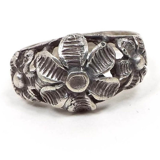 Front view of the retro vintage Boho floral ring. It has a cut out style filigree design with three flowers on top. The middle one is the largest. Each has six line textured petals and a round part in the middle. The silver tone metal has darkened from age to a gray color.