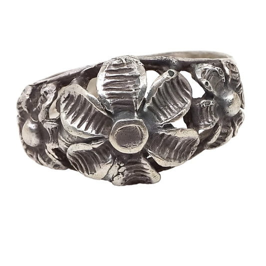 Front view of the retro vintage Boho floral ring. It has a cut out style filigree design with three flowers on top. The middle one is the largest. Each has six line textured petals and a round part in the middle. The silver tone metal has darkened from age to a gray color.