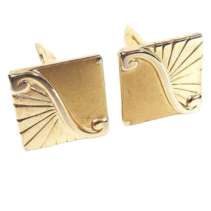 Front view of the Mid Century Vintage Pioneer cufflinks. They are gold tone in color and shaped like squares. The design is split diagonally with a shiny metal area curled at the ends. One side is shiny gold tone metal with diagonal cut lines and the other is matte gold tone in color.