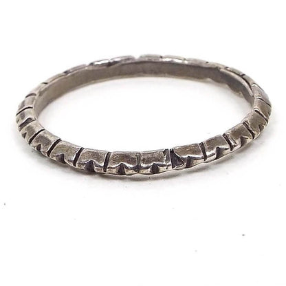 Angled front and side view of the Minimalist thin retro vintage stacking band ring. The metal is darkened silver in color from age. The top edge of the ring slightly bevels outward all the way around the band and has a line and V cut style design. 