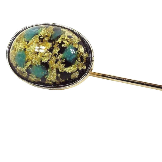 Front view of the Mid Century vintage confetti lucite stick pin. the metal is gold tone in color. There is an oval lucite cab at the top with gold color flakes and spots of mint green and blue.