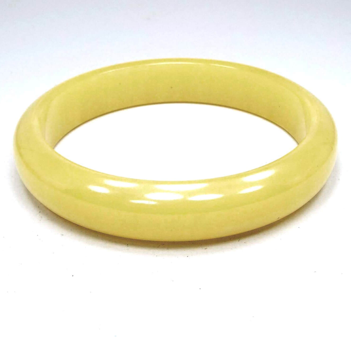 Angled view of the 1950's Mid Century vintage Bakelite bangle bracelet. It is a light yellow in color and has a rounded edge. The inside edge is flat and smooth.