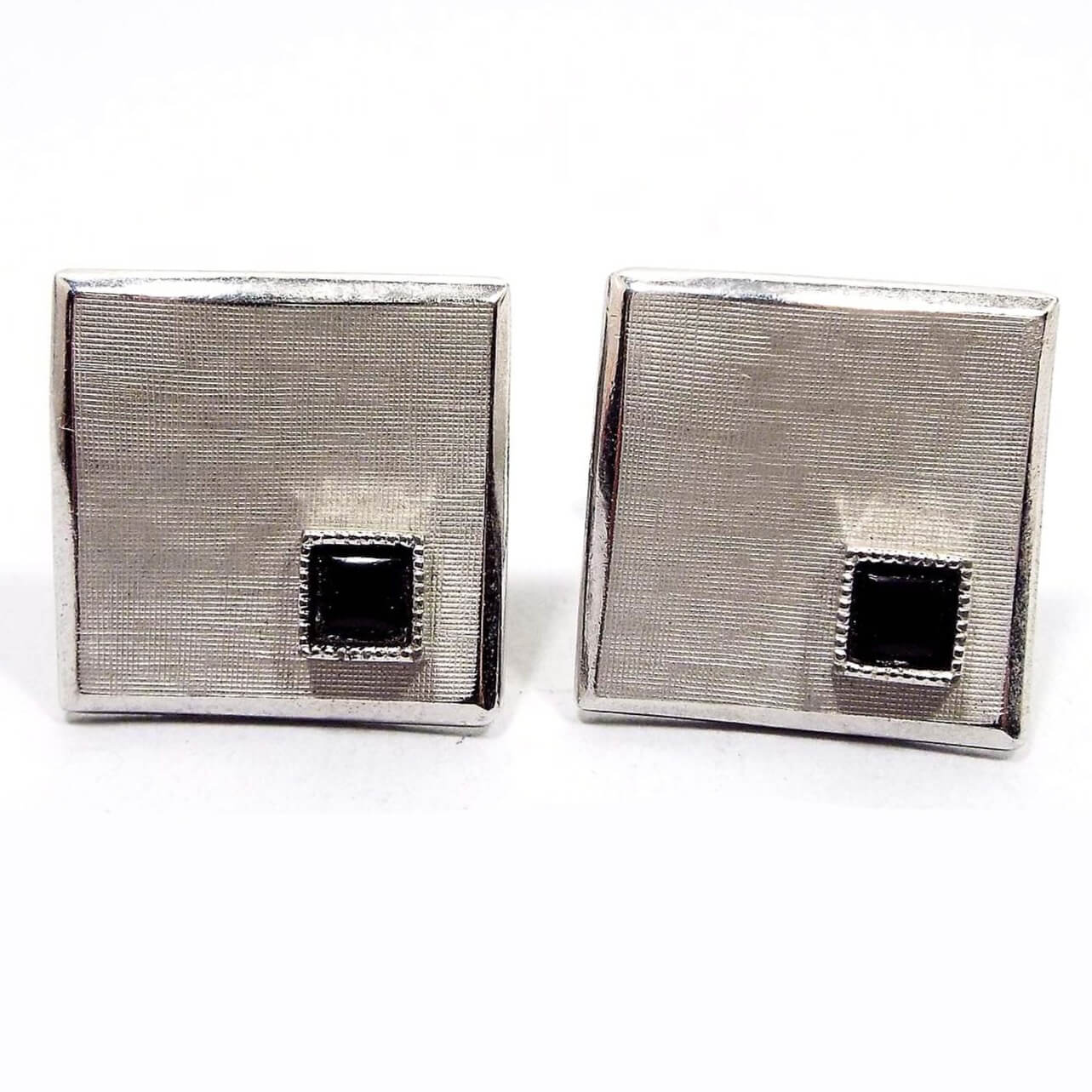 Front view of the Mid Century vintage Swank wavy cufflinks. They are brushed matte silver tone in color. There are small square black glass cabs on one corner. The cufflinks are square shaped but have an abstract wavy style design.