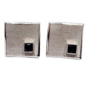 Front view of the Mid Century vintage Swank wavy cufflinks. They are brushed matte silver tone in color. There are small square black glass cabs on one corner. The cufflinks are square shaped but have an abstract wavy style design.
