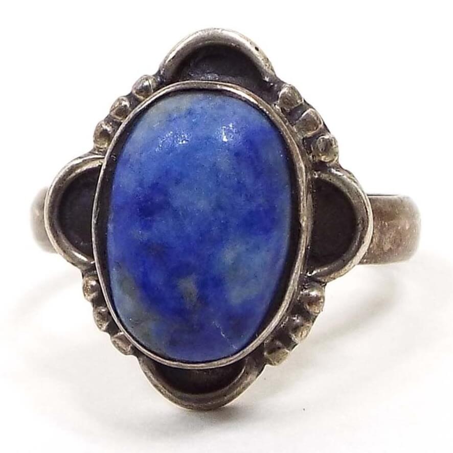 Front view of the retro vintage sterling silver sodalite ring. The sterling is darkened from age. The middle has a large bezel set sodalite gemstone cab that is marbled in shades of denim blue with some flecks of gray. The outer setting has a half moon design at each side with three dots in between them.
