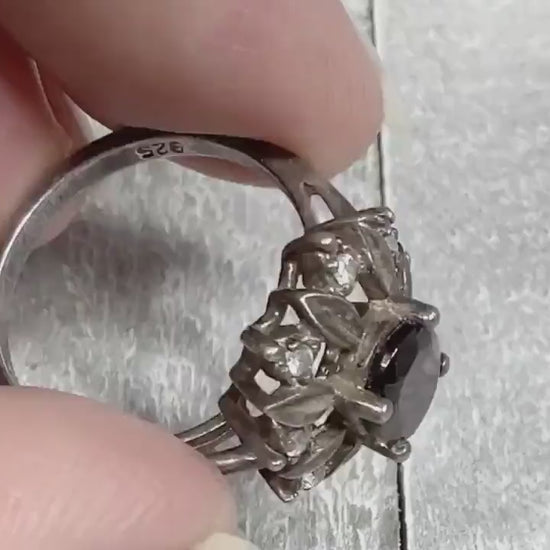 Video of the NV retro vintage sterling silver garnet and CZ ring. The top has a flower pattern with an oval garnet stone in the middle surrounded by metal petals and small round cubic zirconia stones. The video is showing the sparkle and how the stones look as you move around.