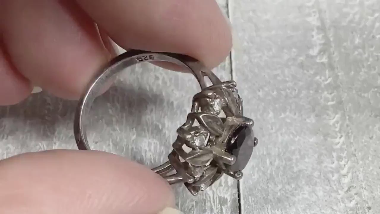 Video of the NV retro vintage sterling silver garnet and CZ ring. The top has a flower pattern with an oval garnet stone in the middle surrounded by metal petals and small round cubic zirconia stones. The video is showing the sparkle and how the stones look as you move around.