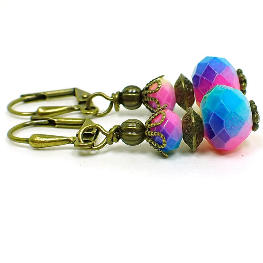 Side view of the rainbow earrings. The metal is antiqued brass in color. There are faceted glass rondelle beads at the top and larger ones at the bottom. They have different vibrant colors of the rainbow blended all the way around the beads.