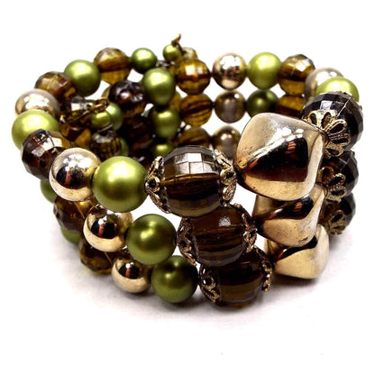 Front view of the Mid Century vintage Fall style memory wire bracelet. It has three rows of plastic chunky beads in metallic green, faceted brown, and metallic gold color. Some of the metallic coating on the beads is worn some for a lighter color in areas.