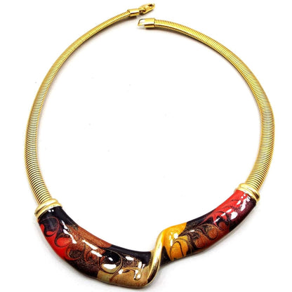 Front view of the retro vintage enameled bib necklace. The metal is gold tone in color. There is omega chain on either side of the necklace in gold tone plated color. The bottom bib area is a U shape with a twist in the middle. There are swirls of black, red, copper, olive green, and gold colors on the bib area. There is a snap lock clasp at the end.